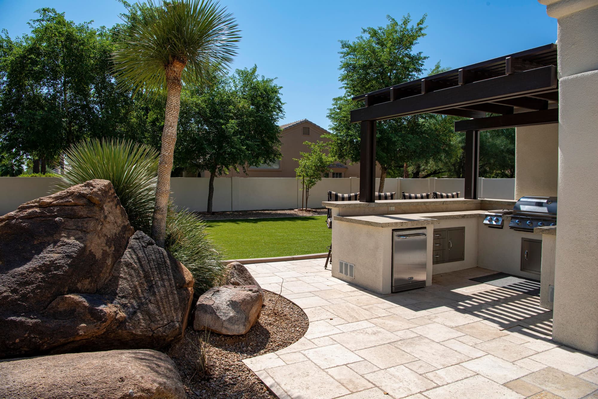 Outdoor kitchen under a steel pergola beside a paver patio