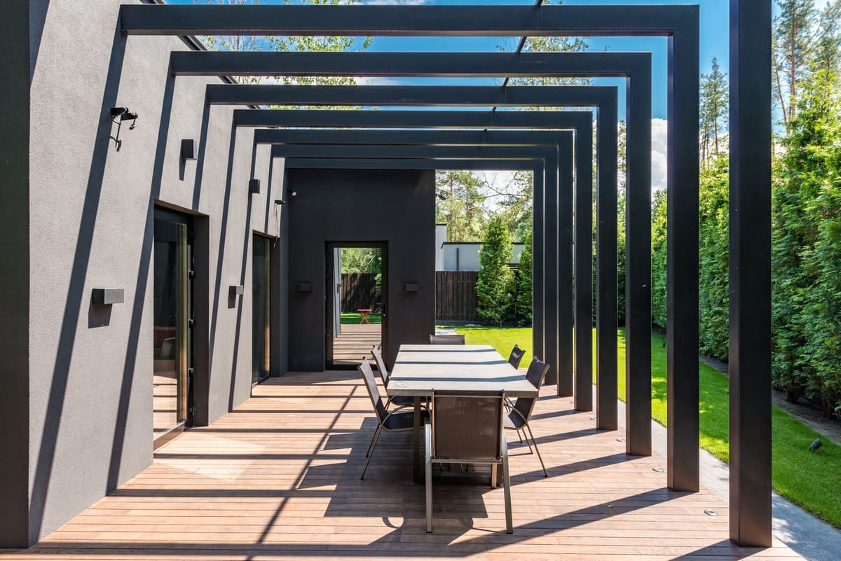 Dark steel-frame pergola over an outdoor dining table on a wood deck