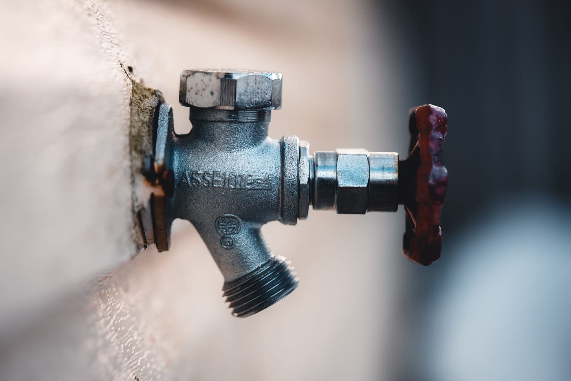 Outdoor hose bib with a red handle on a house wall